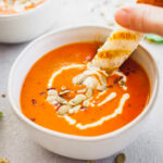 a hand dipping a fontina grilled cheese sandwich into a bowl of homemade tomato soup.