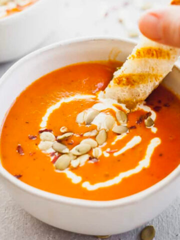 a hand dipping a fontina grilled cheese sandwich into a bowl of homemade tomato soup.