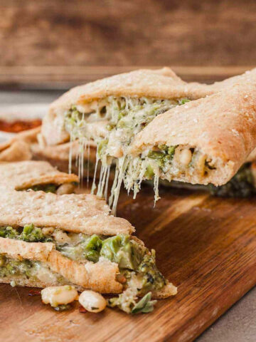 side view image of vegetarian calzone on cutting board cut into.
