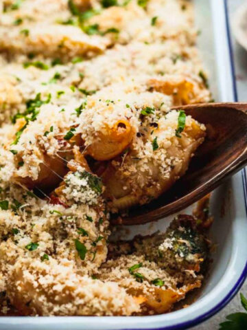 Sun Dried Tomato and Broccoli Unstuffed Shells in casserole dish with wooden spoon scooping out some.