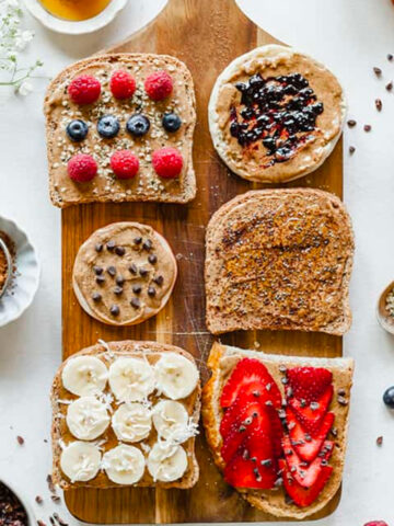 top view image of almond butter toast bar with ingredients on top wooden board and bowls of ingredients on white table.