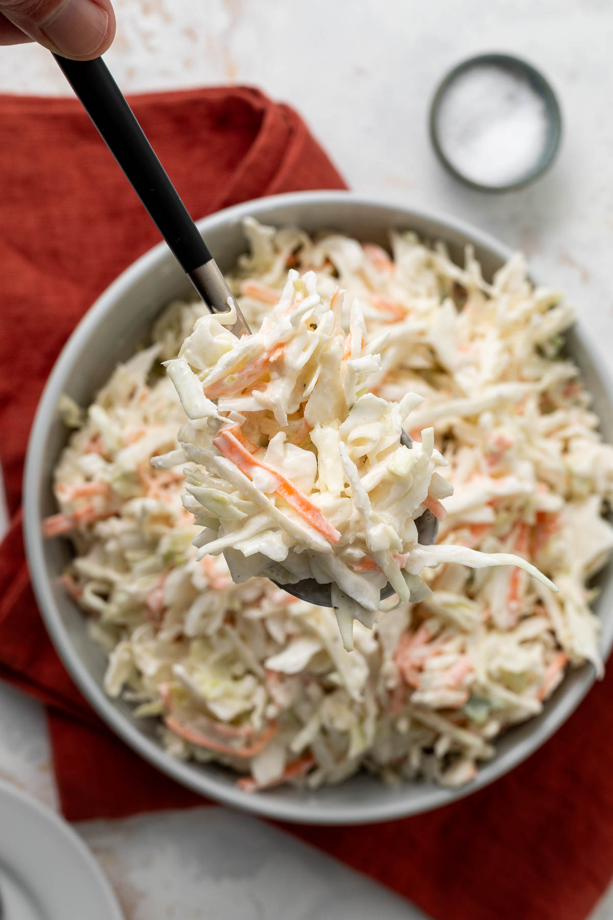 A bowl of no-mayo coleslaw on a red linen napkin with a spoon lifting up a bite.