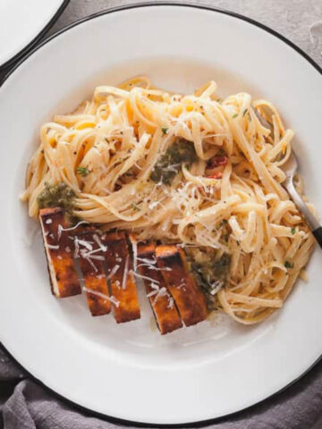 cajun tofu sliced over fettuccine alfredo on a white plate.