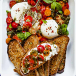 white casserole dish with burrata with tomatoes pesto and toast with a metal spoon