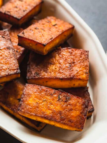 close up image of cooked tofu in white dish with stripe kitchen towel