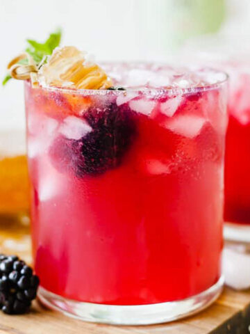 blackberry gin smash in a glass with a blackberry and honeycomb