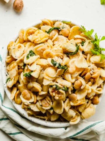 top view full bowl of orecchiette with spinach and butter beans with striped dish towel.