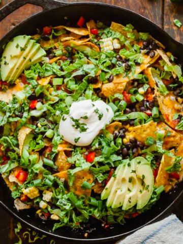 overhead photo of nachos in a cast iron skillet on a wood table.
