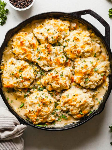 topview image of biscuits topped vegetarian pot pie in a cast iron pan with spices in a bowl.