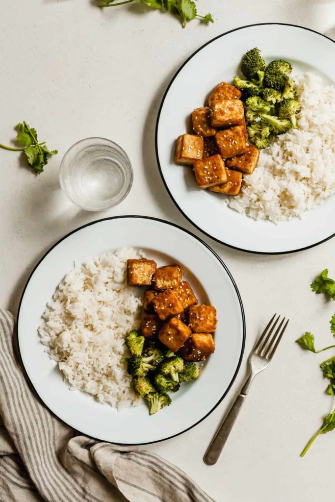 two white plates with crispy tofu, broccoli, and rice