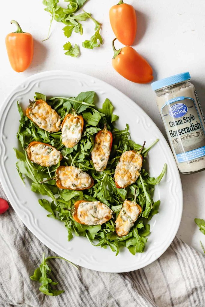 cream cheese stuffed mini peppers on a plate of greens with peppers and horseradish