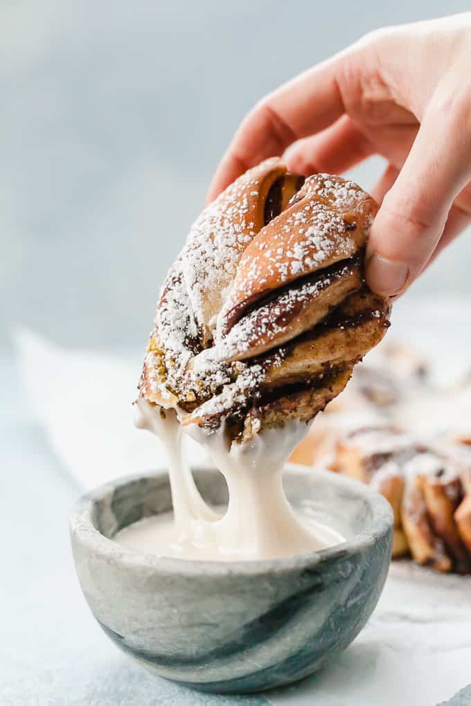 a hand dipping a piece of chocolate pistachio christmas star bread in vanilla icing dip