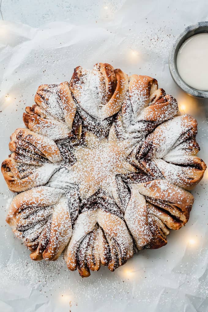 chocolate pistachio christmas star bread on a white background with twinkle lights and a bowl of vanilla icing dip