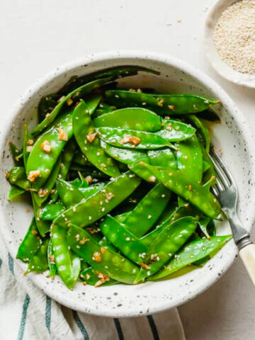 garlic ginger snow peas in a white bowl on a white background.