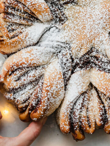 a hand grabbing a spoke from chocolate pistachio christmas star bread