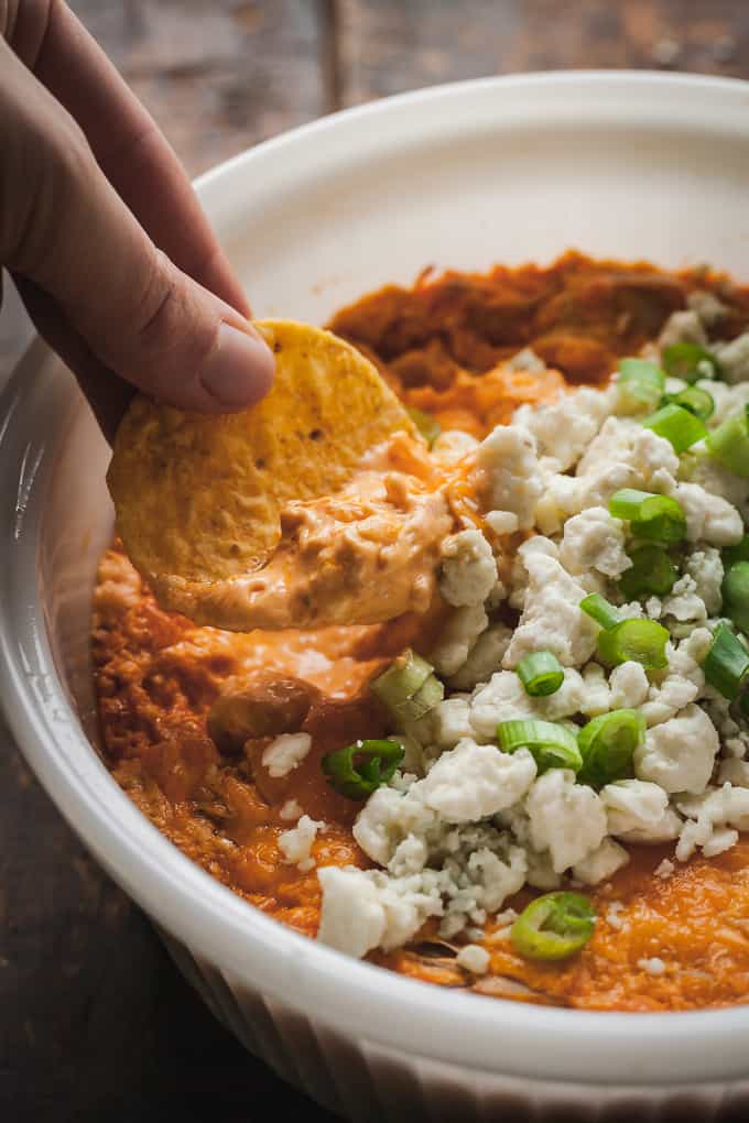 a hand dipping a tortilla chip in a white dish of vegetarian buffalo dip