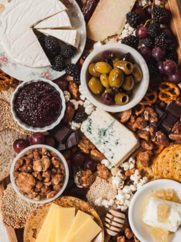 a bowl of mixed olives on a cheese board with fruit and jam.