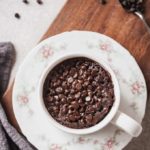 vegan chocolate mug cake in a white mug on a pink flower plate on a wood cutting board