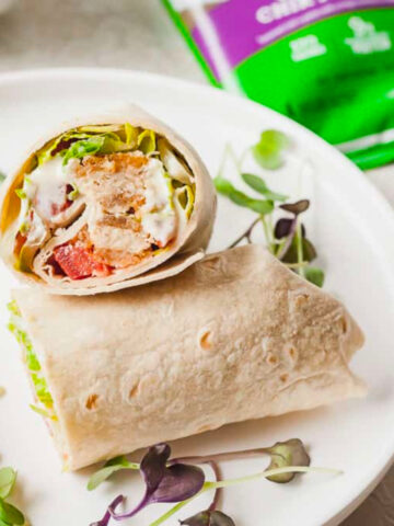 a chik'n caesar wrap cut in half on a white plate.