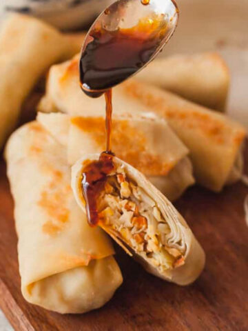 a stack of baked vegetable egg rolls, one cut in half with sauce being poured over it.