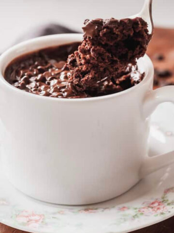 a hand taking a spoonful of microwave mug cake out of a white mug.