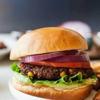 a black bean burger with tomato, lettuce, onion, and avocado on a bun