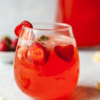 a glass of strawberry lemonade with a pitcher in the background