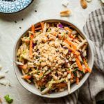 a bowl of Asian slaw with a small dish of black sesame seeds and a cloth napkin