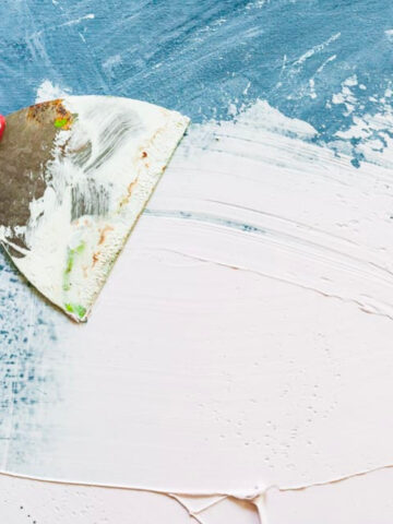 joint compound being spread on a wooden board.