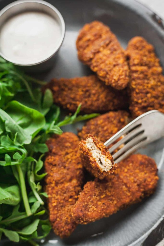spicy meatless tenders on a plate with arugula and ranch, with a fork in a cut piece