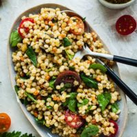 israeli couscous salad in a platter with a spoon and fork