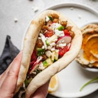 a hand holding a double bean pita sandwich
