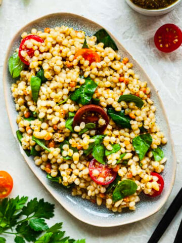 israeli couscous salad in a platter with a spoon and fork.