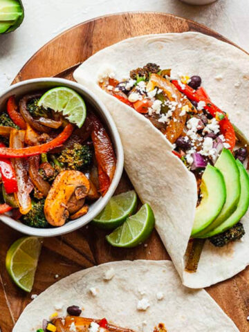 vegetarian fajitas on a wood platter with avocado, a bowl of veggies, and a glass of beer.