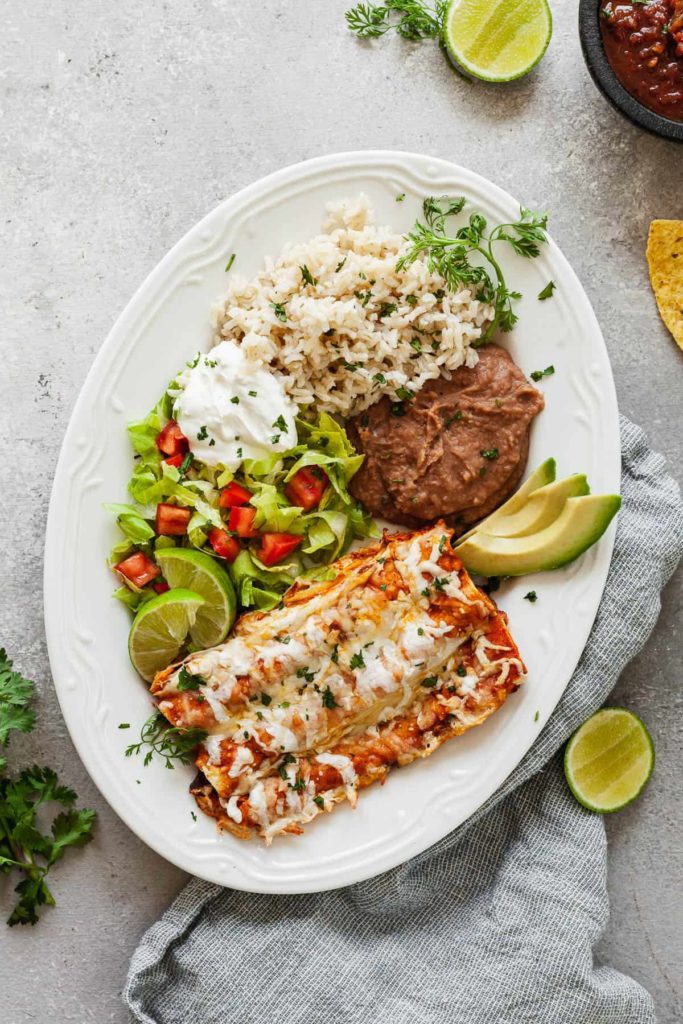 a large plate of easy cheese enchiladas with rice, beans, salad, and sour cream