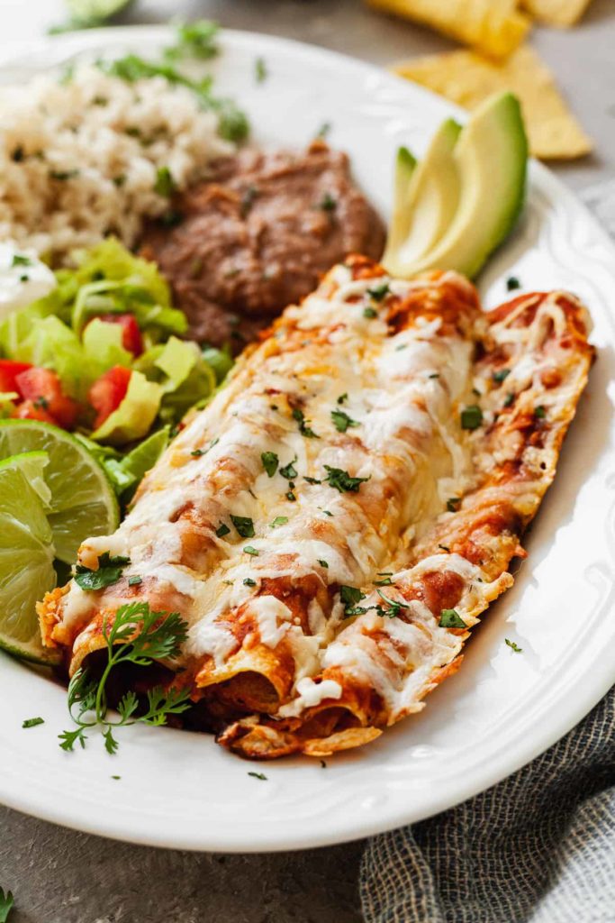 cheese enchiladas on a plate with salad, rice, and beans