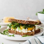 a peach, arugula, and goat cheese sandwich on a white plate with a striped napkin
