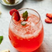 a glass of strawberry vodka lemonade cocktail with honey, strawberries, and lemons