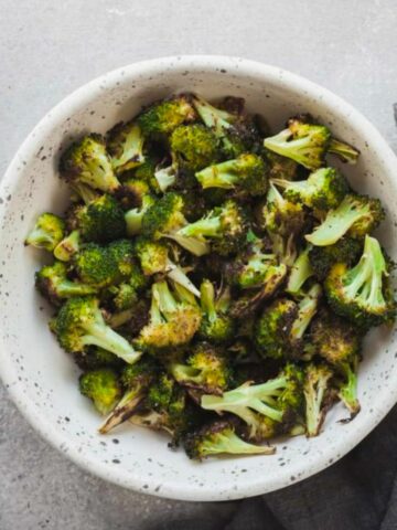 Oven roasted broccoli in a white speckled bowl.