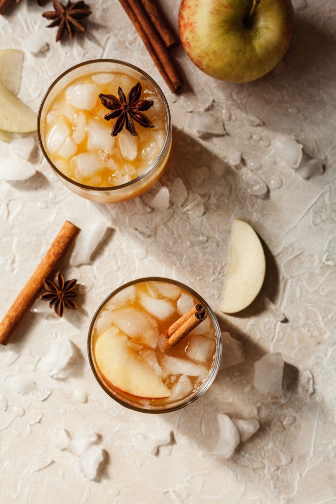 overhead photo of two apple cider whiskey cocktails with cinnamon sticks, ice, and apple slices