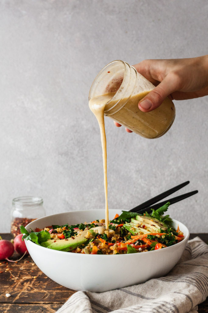 a hand pouring creamy tahini dressing on a kale salad