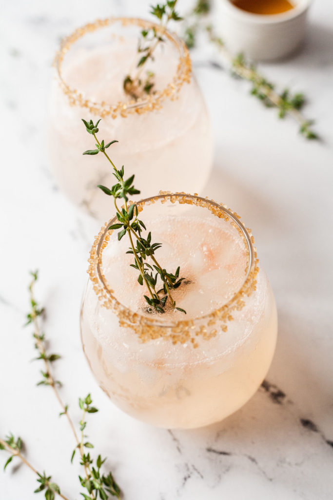 two grapefruit vodka drinks with sprigs of thyme on a marble background