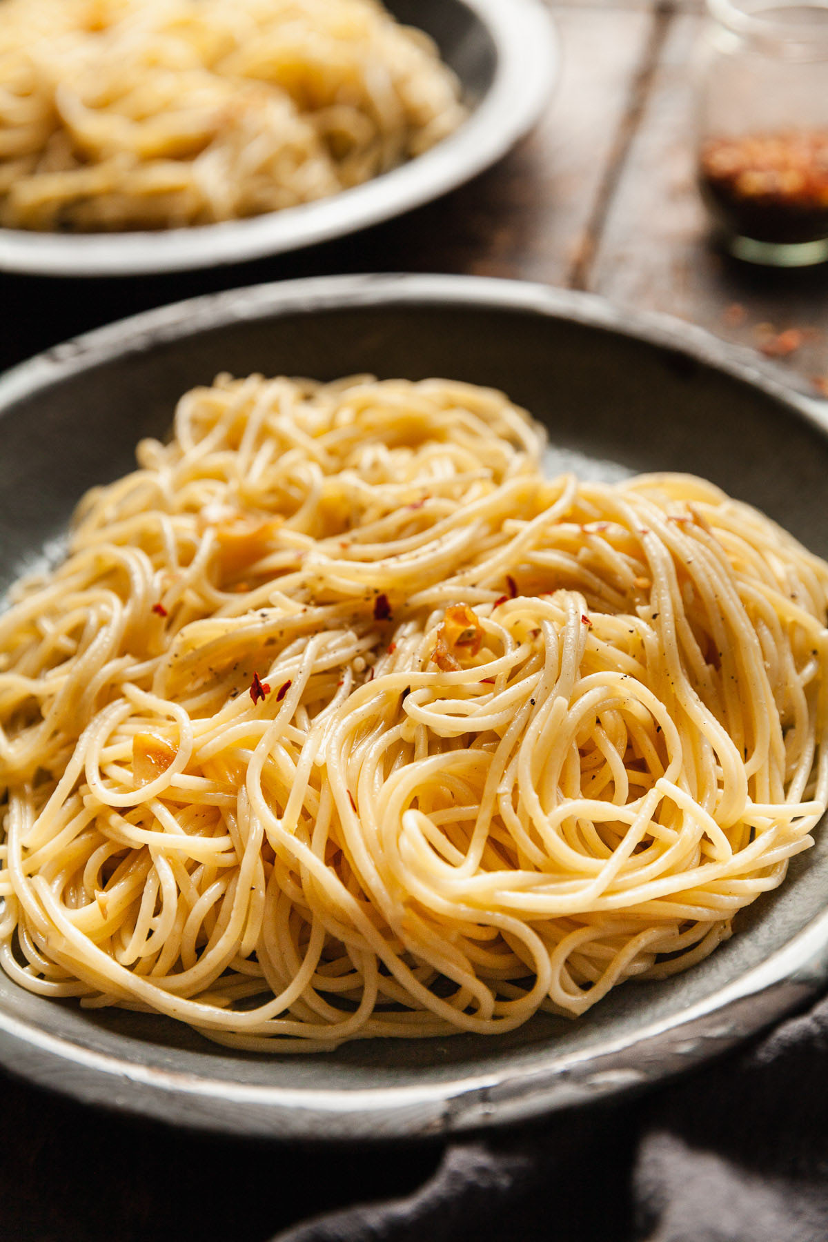 two blue plates on a wood table with spaghetti aglio e olio