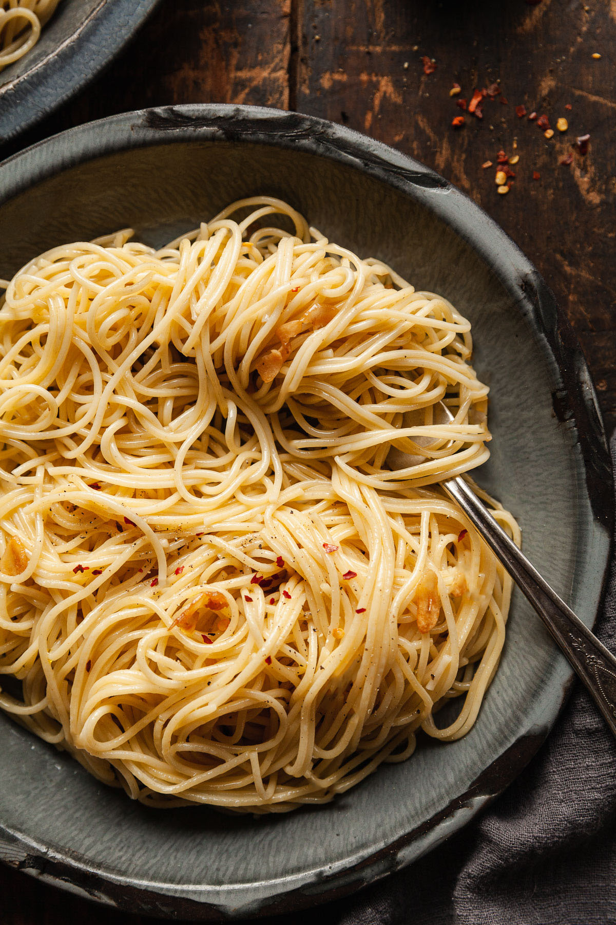 a fork twirling spaghetti with garlic oil on a blue plate.