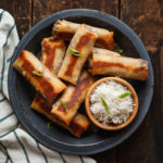 vegetarian baked southwest egg rolls on a blue plate with white rice in a wood bowl