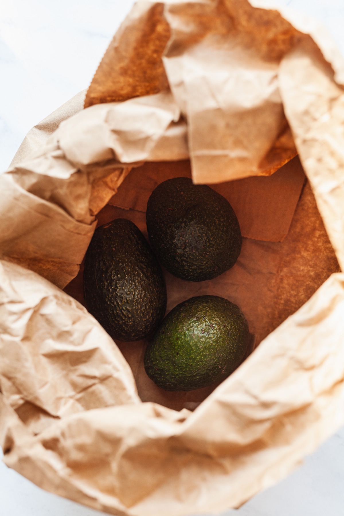 three avocados in a brown grocery bag.