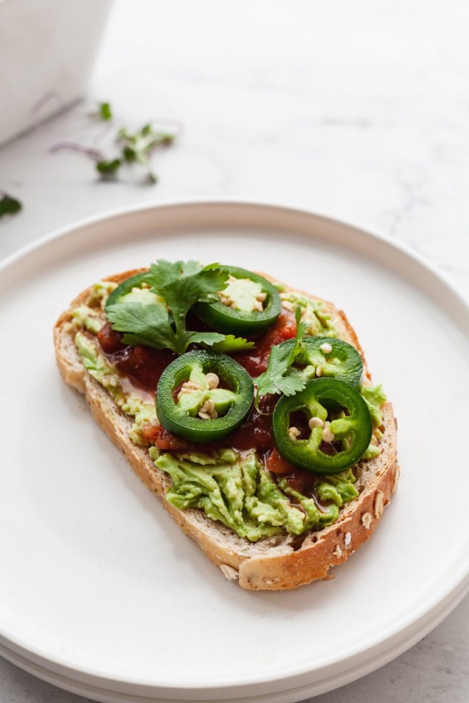 a slice of avocado toast topped with salsa and jalapeno slices