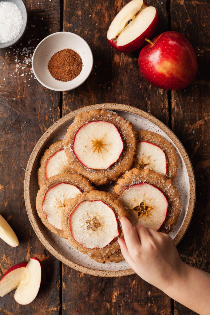 a child's hand reaching in to grab an apple cookie from a plate