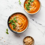 two bowls of carrot ginger soup with peanuts