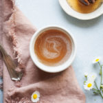 a small bowl of honey syrup with a pink napkin, flowers, and honey wand